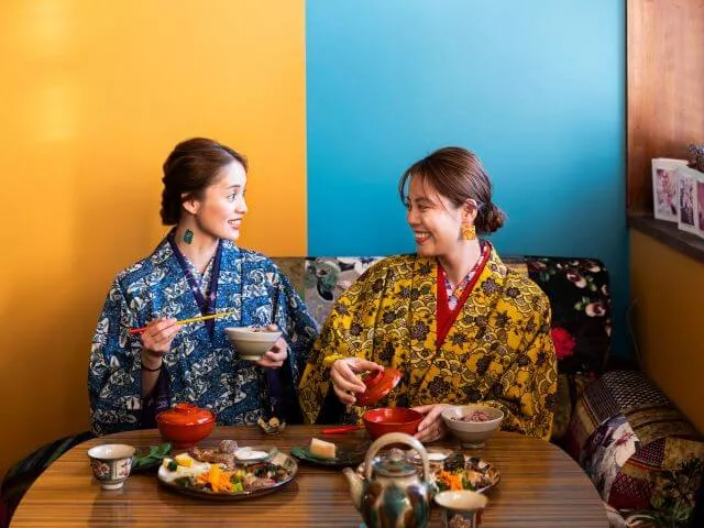 鮮やかな琉装を着用して室内で仲良く並んで座る女性2人の記念写真