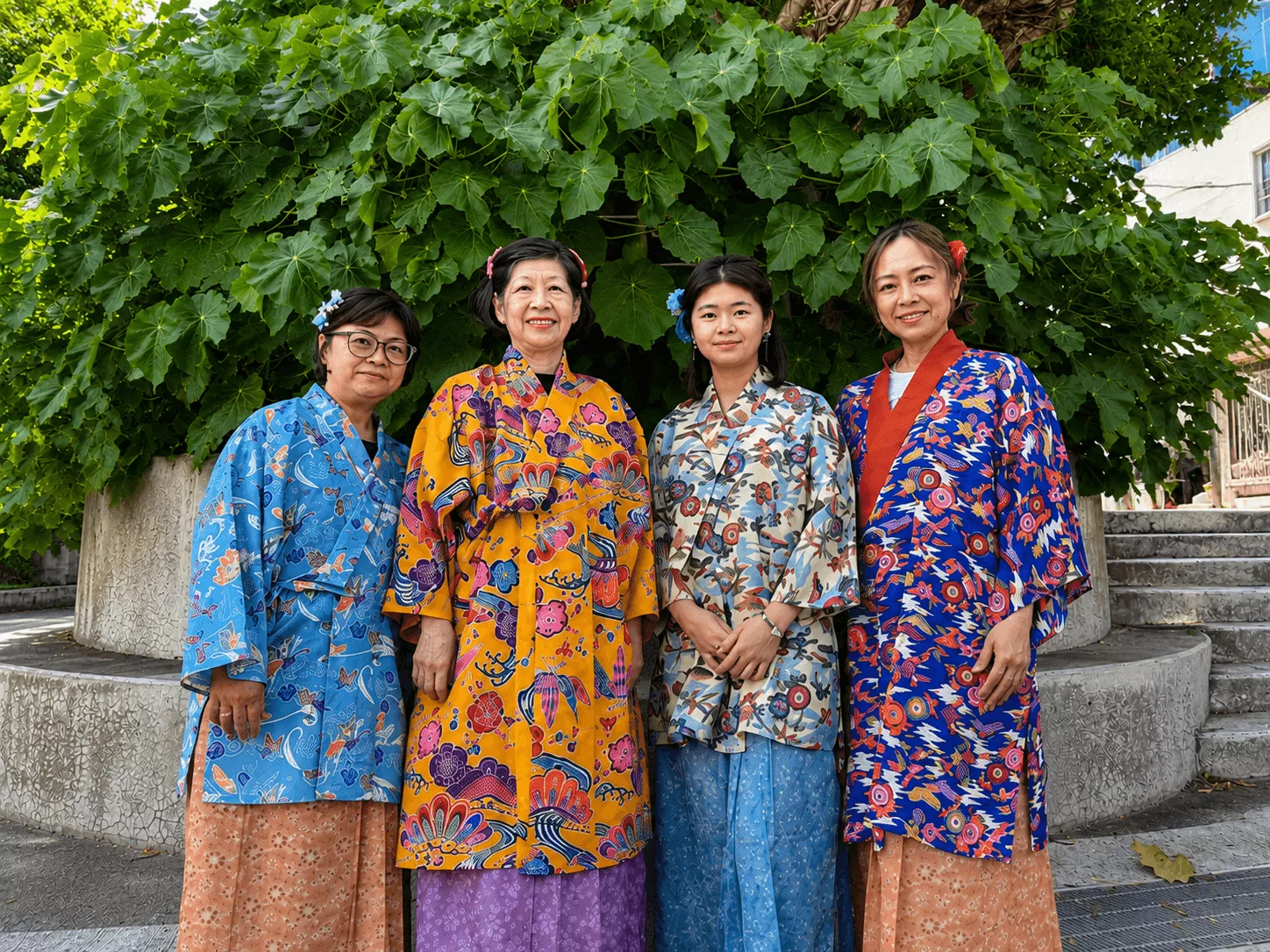 沖縄の街並みで多様な琉装を着て笑顔で見つめ合う4人のグループ写真