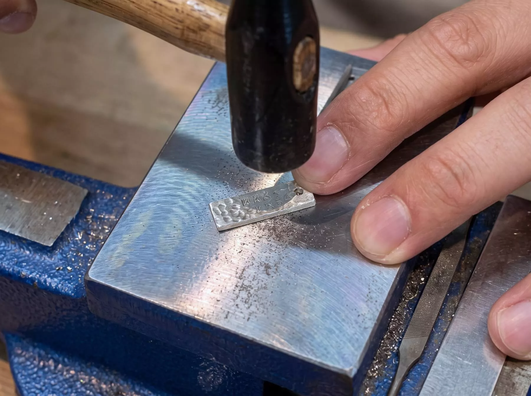 作業台でタガネと金づちを使いシルバーパーツへの刻印や成形加工を行う手作り体験の様子